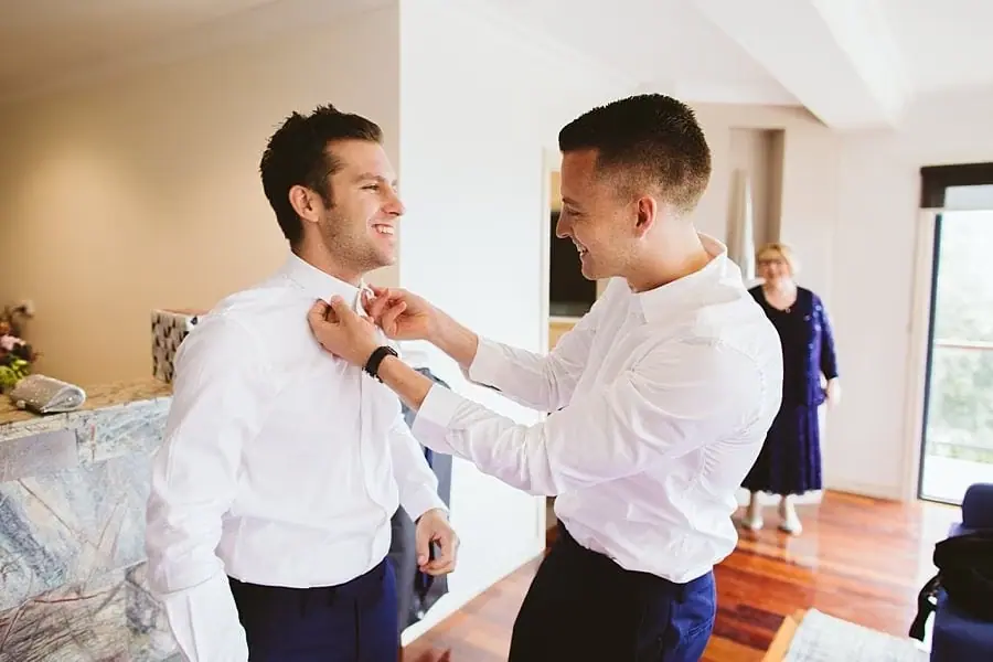 Man helping another man fasten a bow tie.