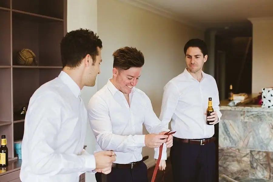 Men in white shirts preparing bow ties and holding drinks.