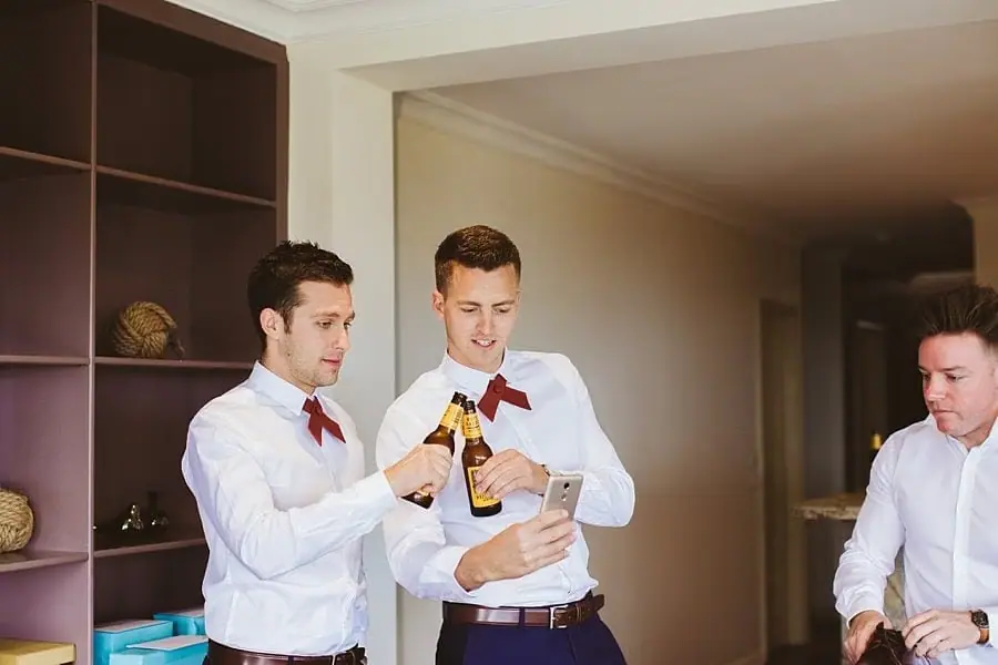 Men in white shirts and red bow ties raising their drink bottles.