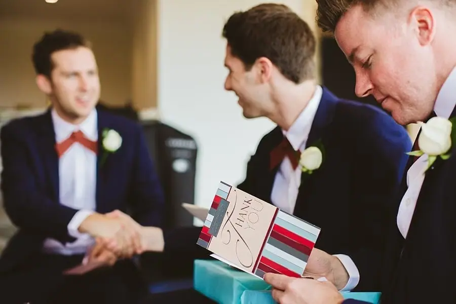 Suited man looking down at a card while companions smile beside him.