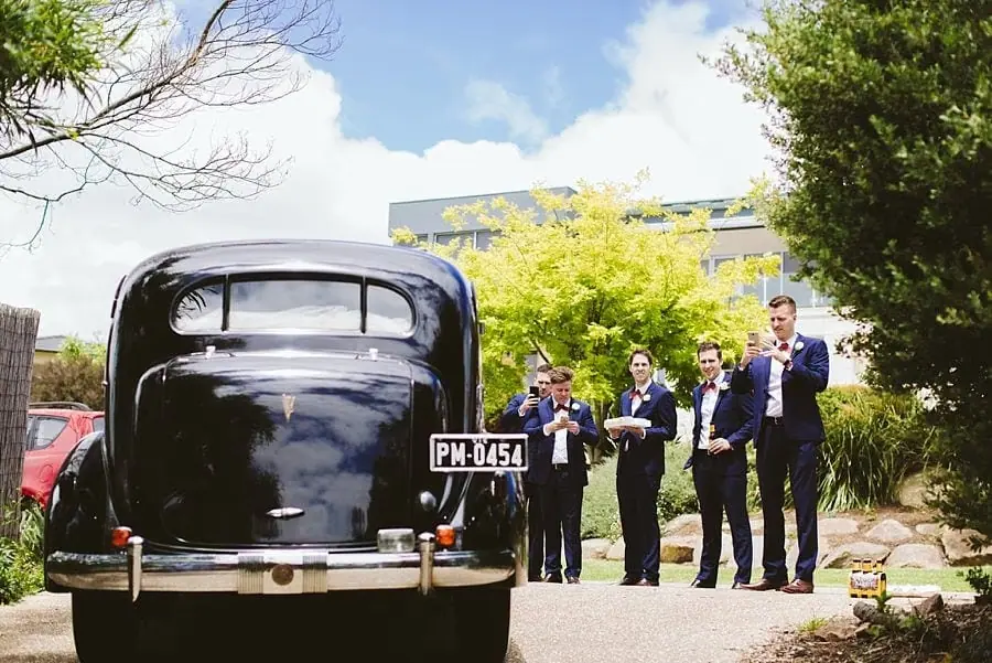 Suited men standing beside the rear of a vintage black car.