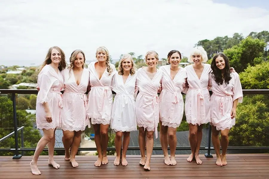 Eight women in pale robes posing in a row on a wooden deck.