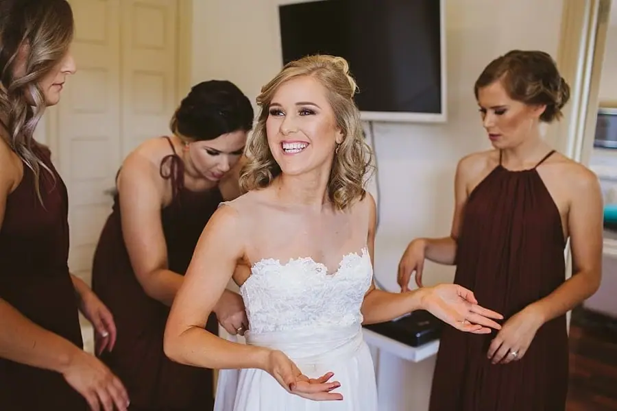 Bride smiling as women help adjust her dress.