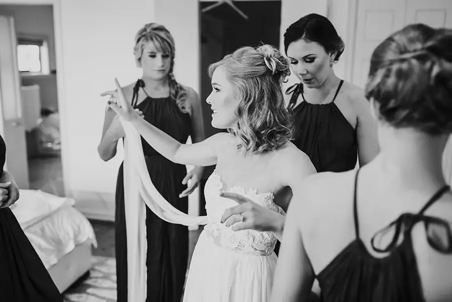 Black-and-white photograph of women helping arrange the bride's clothing.