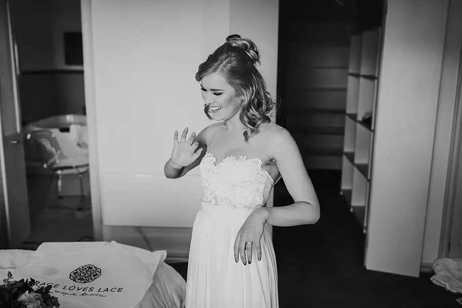 Black-and-white photograph of the bride holding one hand near her face while smiling.