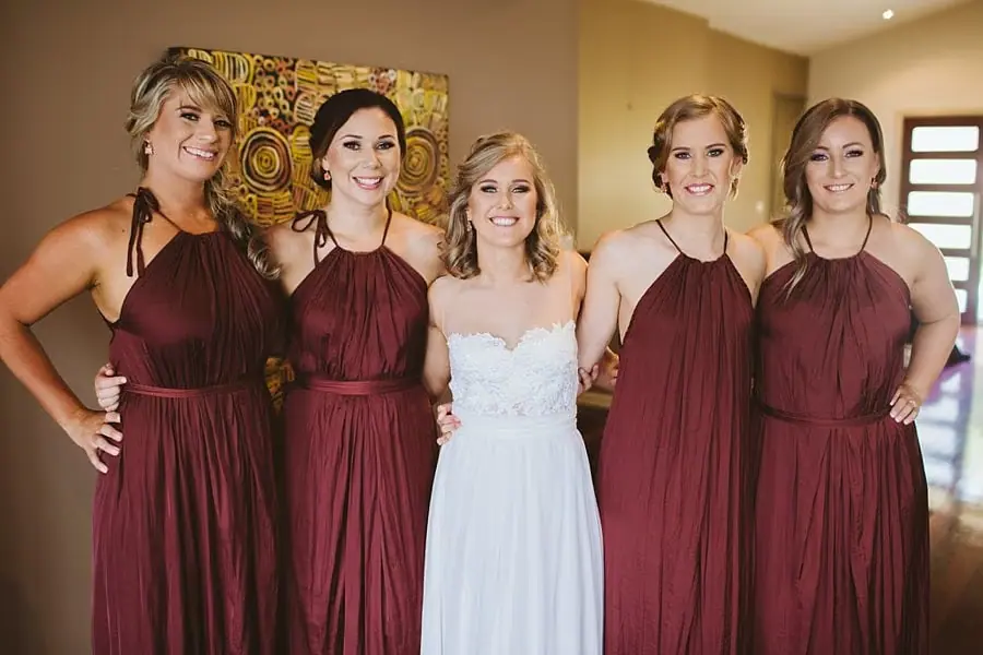 Bride posing between four women in burgundy dresses.