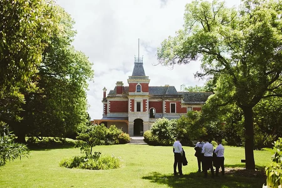 People walking across a lawn toward a large historic brick house.