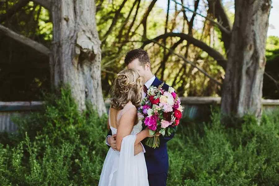 Bride and groom embracing beneath a large tree.