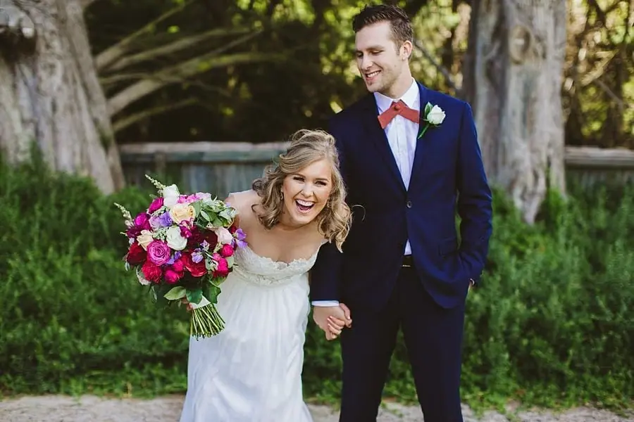 Bride laughing beside the groom with a bouquet in her hand.