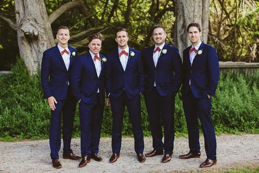 Five men in navy suits and red bow ties standing in a row.