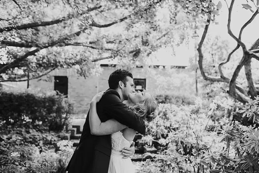 Black-and-white photograph of the couple kissing beside a tree.