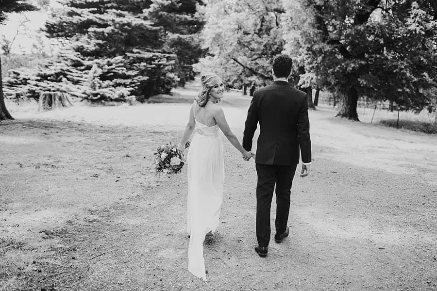 Black-and-white photograph of the bride and groom walking away along a path.