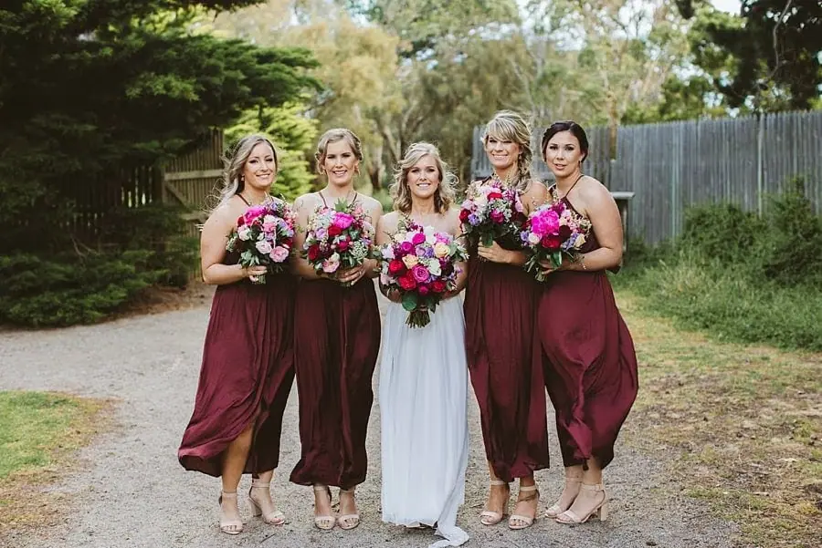 Bride walking alongside four women in burgundy dresses with bouquets.
