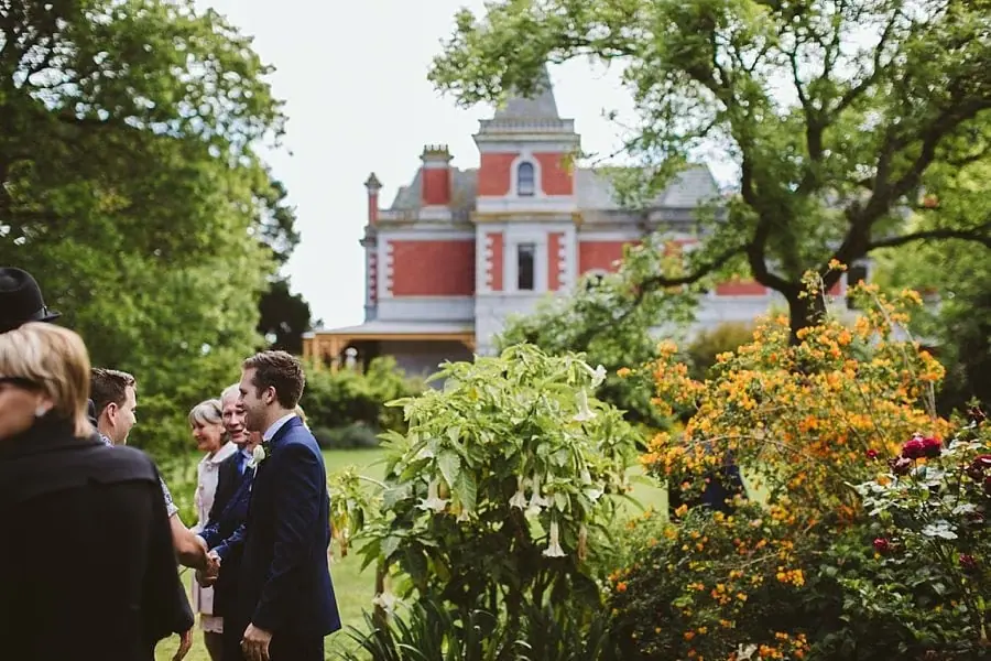 Wedding guests chatting in a garden with a historic house behind them.