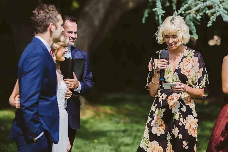 Woman in a floral dress reading into a microphone beside the couple.