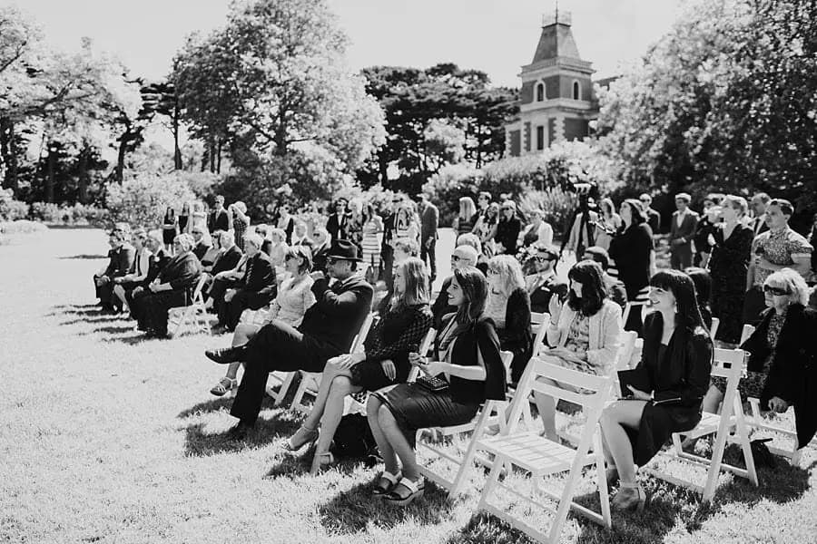 Black-and-white photograph of guests seated on a lawn beside a historic house.