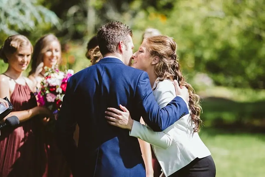 Woman leaning toward the groom while speaking into a microphone.