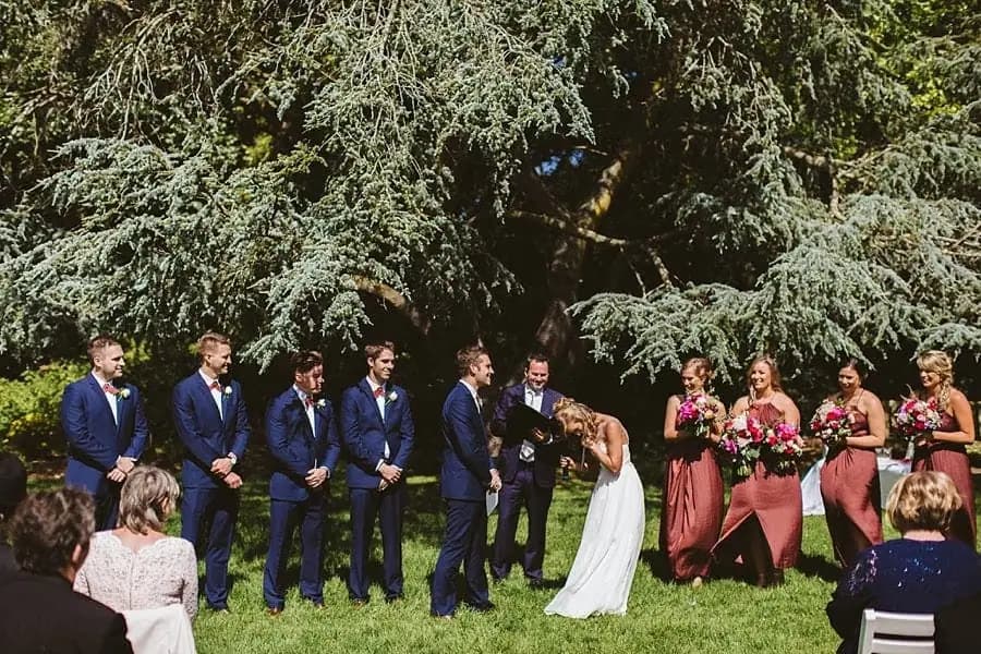 Bride bending forward and laughing while the wedding party watches.