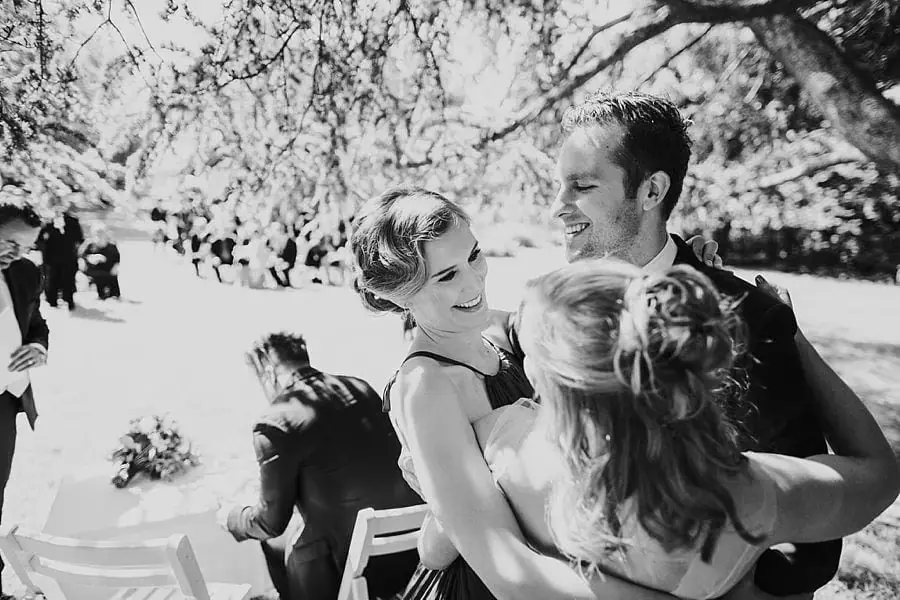 Black-and-white photograph of the groom being greeted by two smiling women.