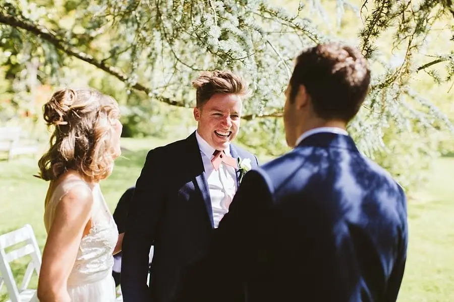 Bride and groom chatting with a smiling suited man.