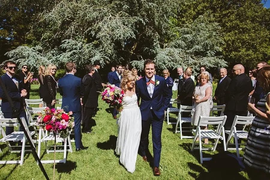 Bride and groom smiling as they walk hand in hand between wedding guests.