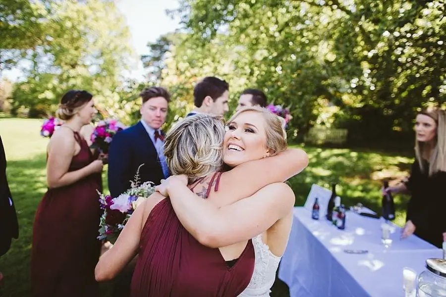 Bride embracing a woman in a burgundy dress.