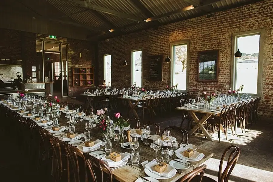 Long reception tables set inside a brick-walled room with tall windows.