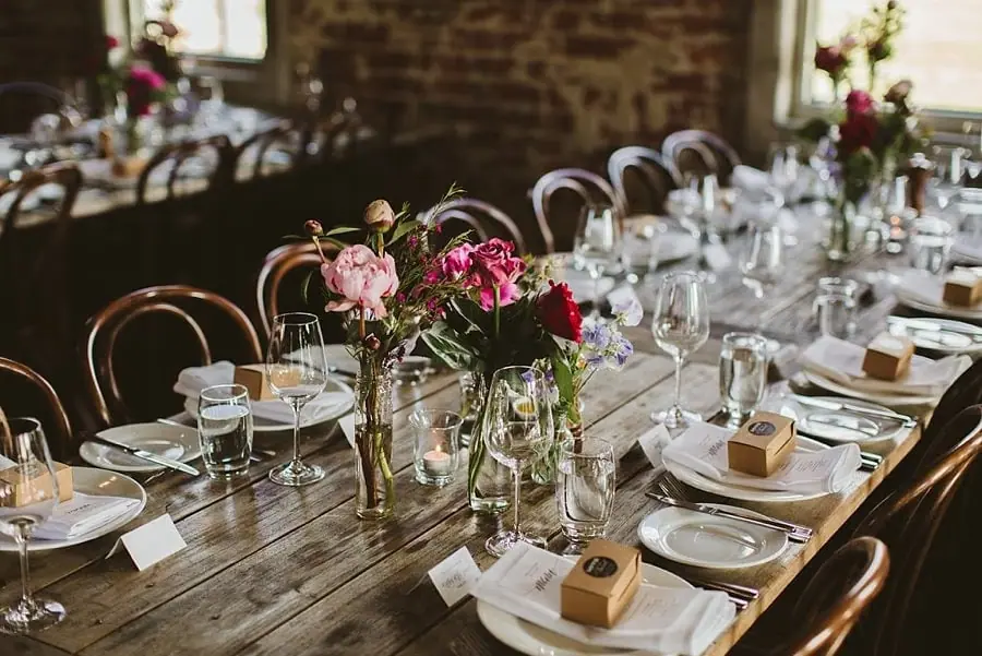 Pink flowers and glassware arranged along a wooden reception table.