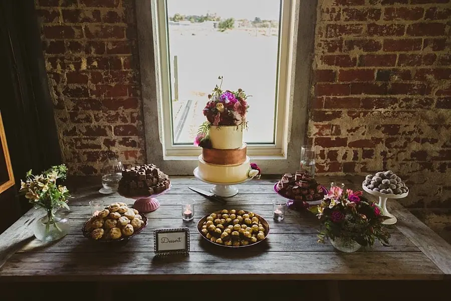 Tiered flower-decorated cake and bite-sized sweets arranged beneath a window.