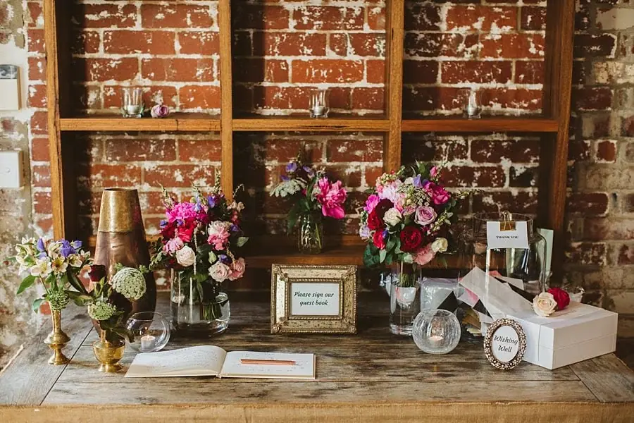 Flowers, glassware and a guest book displayed on a wooden table.