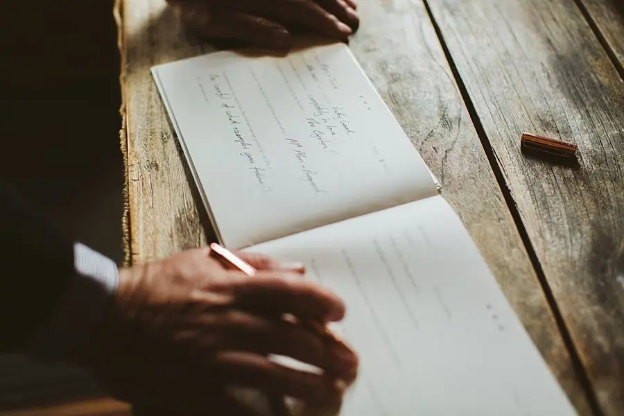 Close-up of someone writing in an open guest book.