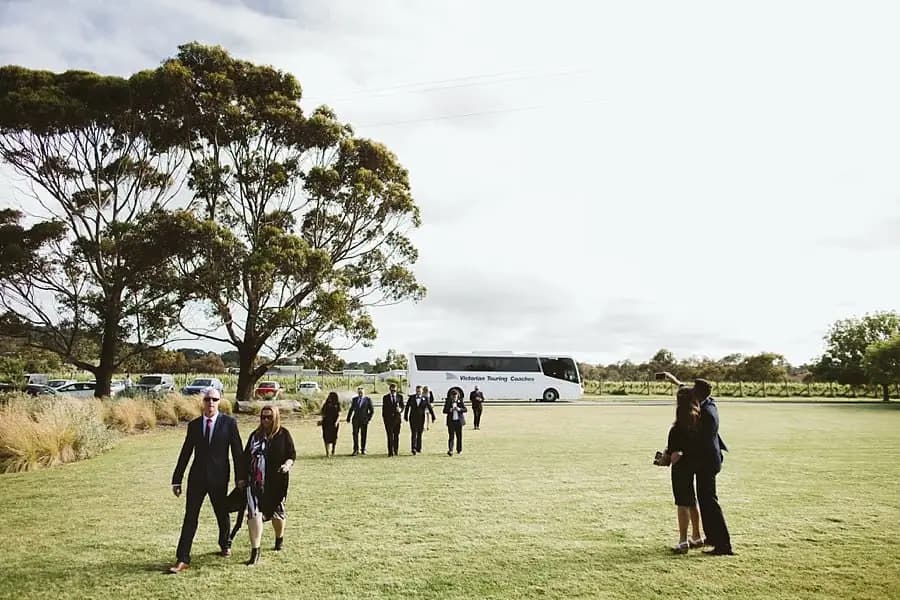 Wedding guests crossing a lawn with a coach parked in the background.