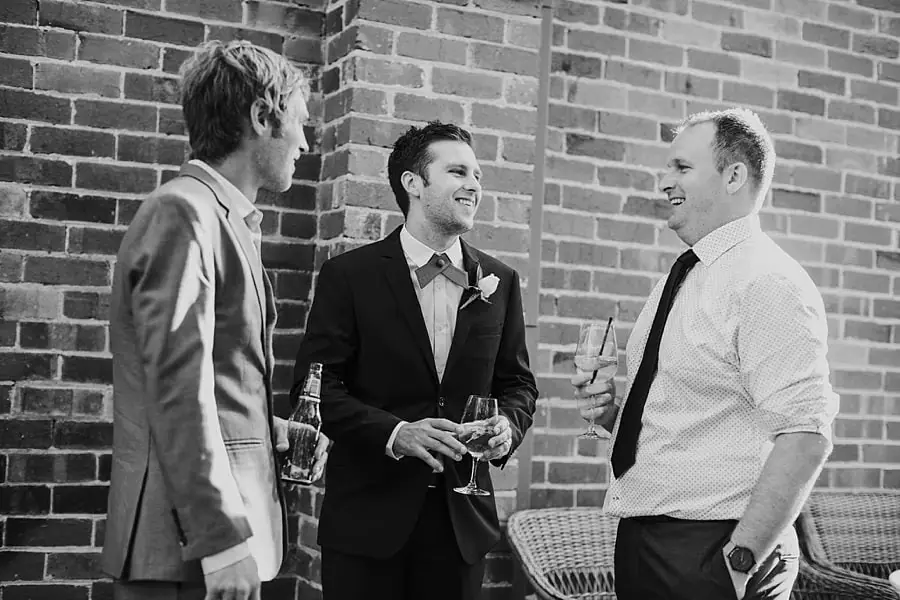 Black-and-white photograph of men chatting beside a brick wall.