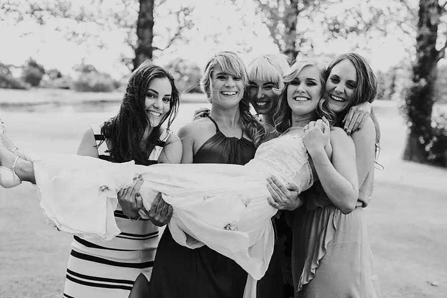 Black-and-white photograph of women holding the laughing bride horizontally.