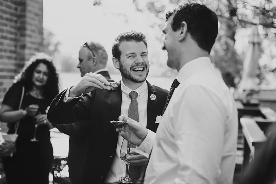 Black-and-white photograph of smiling guests chatting with drinks.