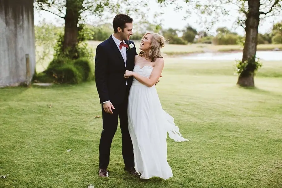 Bride and groom smiling at each other on a green lawn.