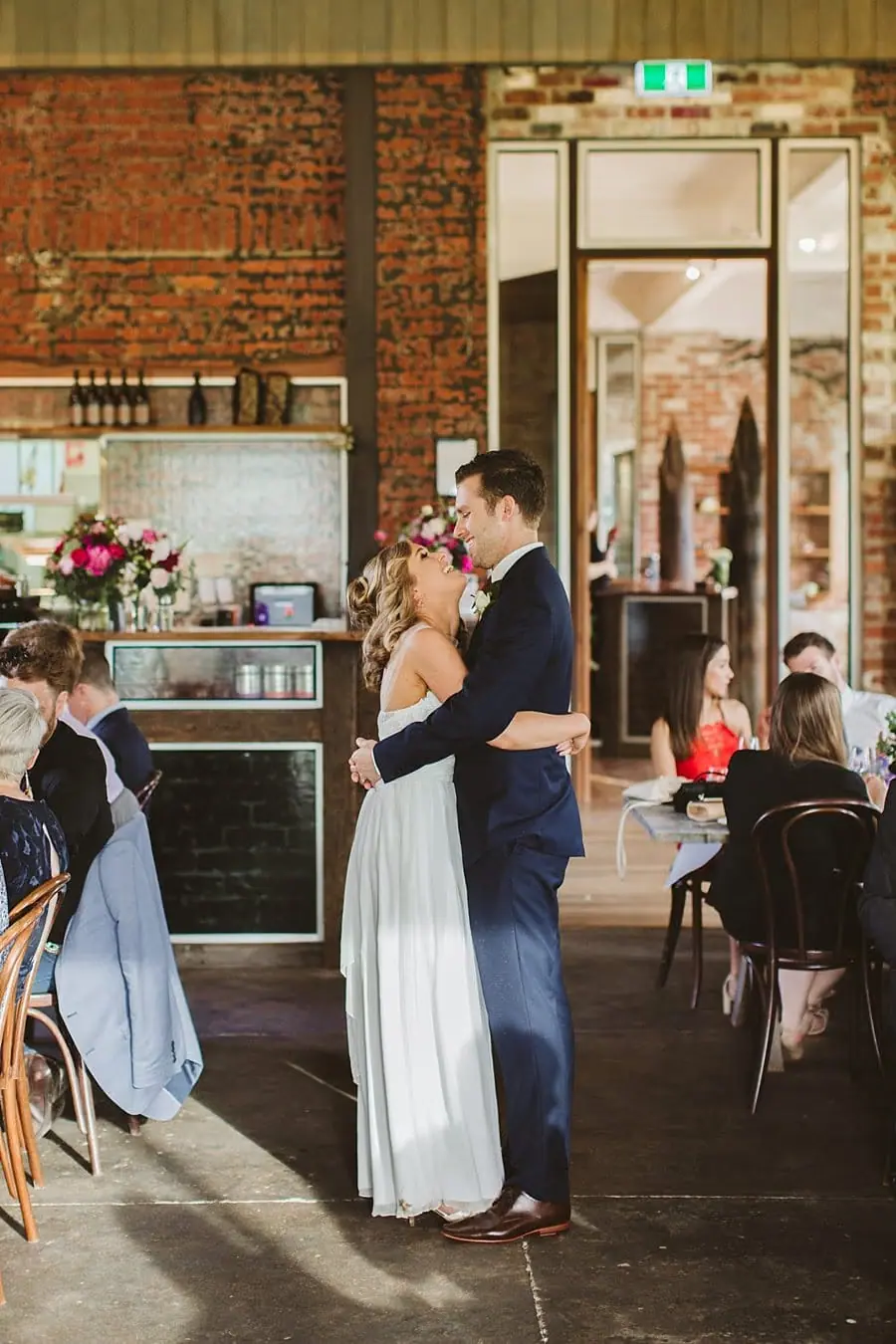 Bride and groom embracing beside a brick wall in the reception room.