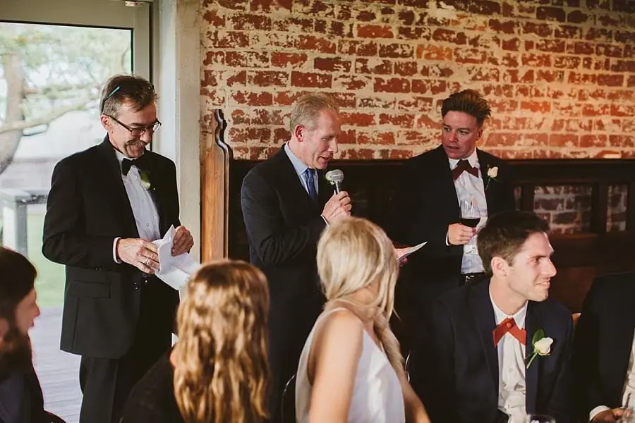 Three suited men standing together during reception speeches.
