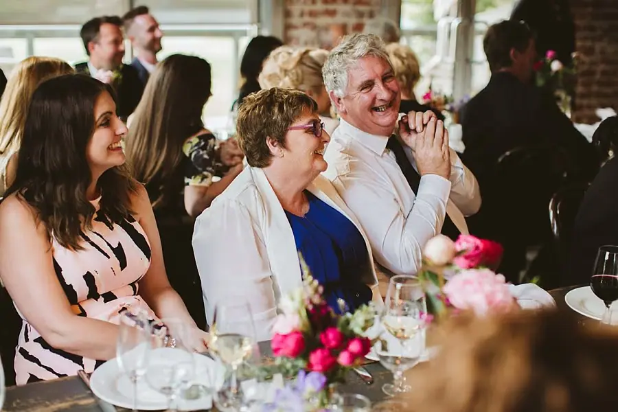 Three women laughing together at a flower-decorated reception table.