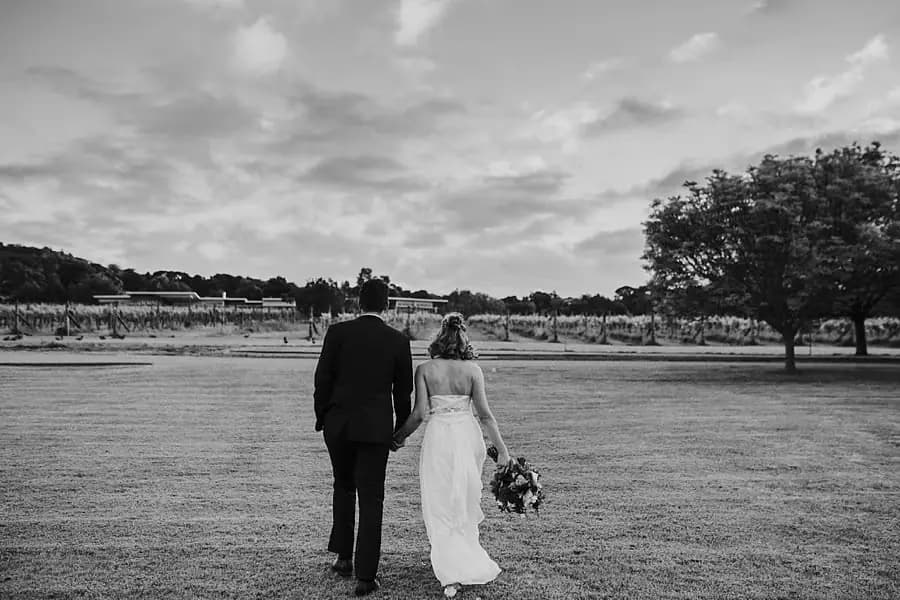 Black-and-white photograph of the couple walking away across an open field.