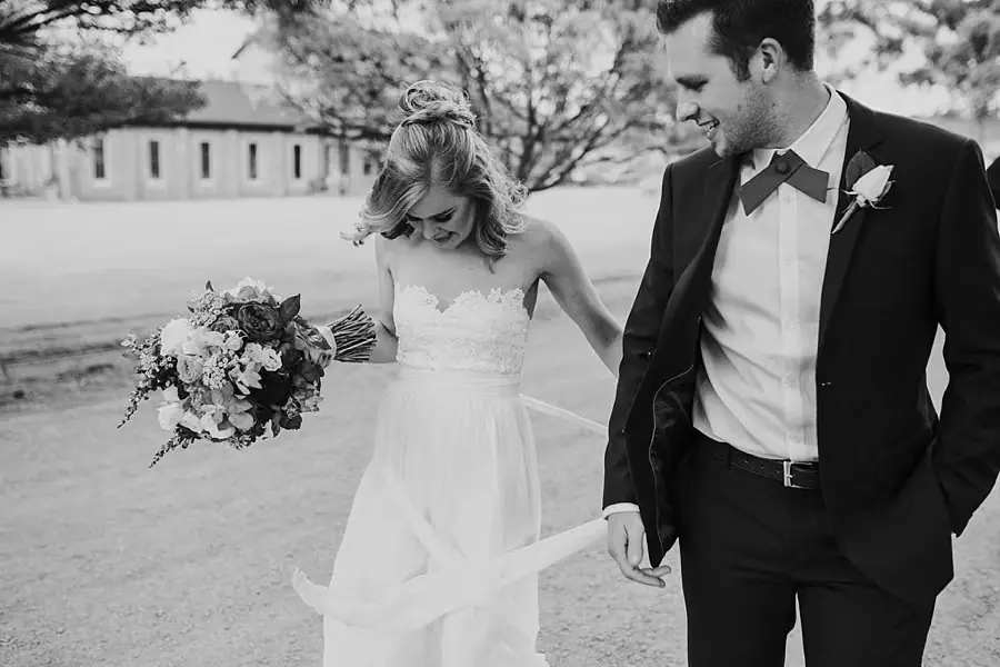 Black-and-white photograph of the bride lifting her skirt as she walks beside the groom.