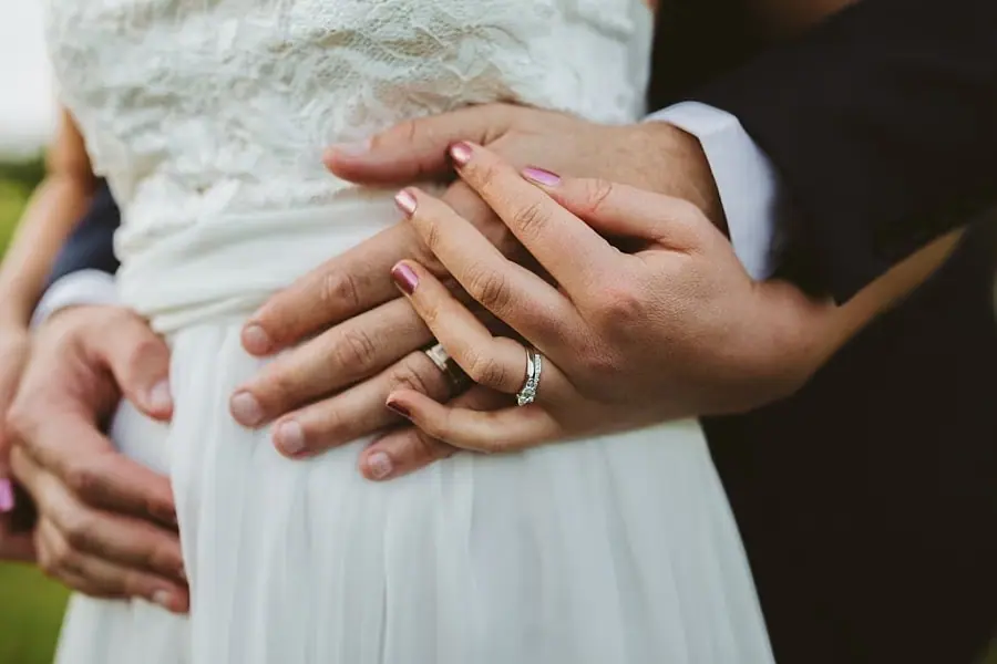 Close-up of the couple's joined hands and wedding rings against the bride's dress.