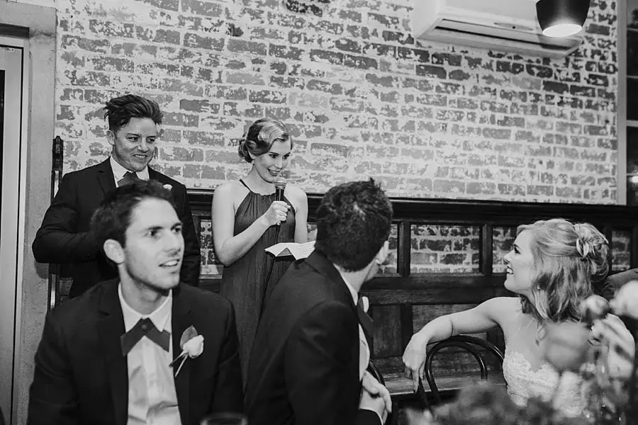 Black-and-white photograph of a suited man and woman giving speeches beside seated guests.