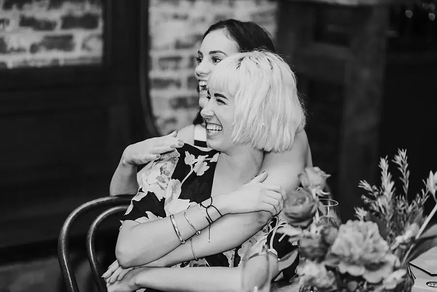 Black-and-white photograph of two women embracing while seated at their table.
