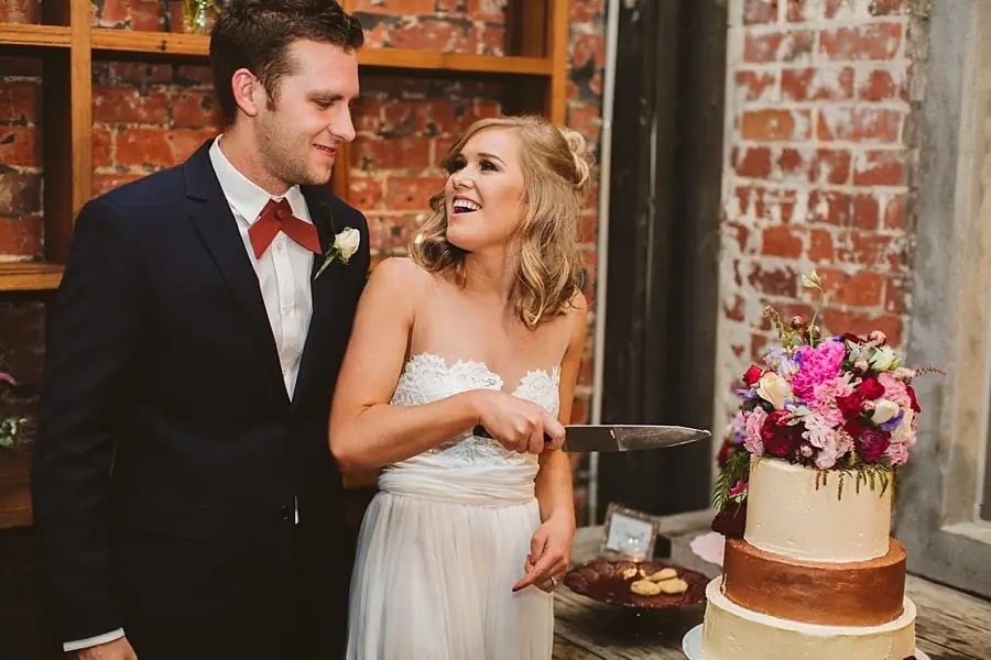 Bride laughing beside the groom while holding a knife near their wedding cake.