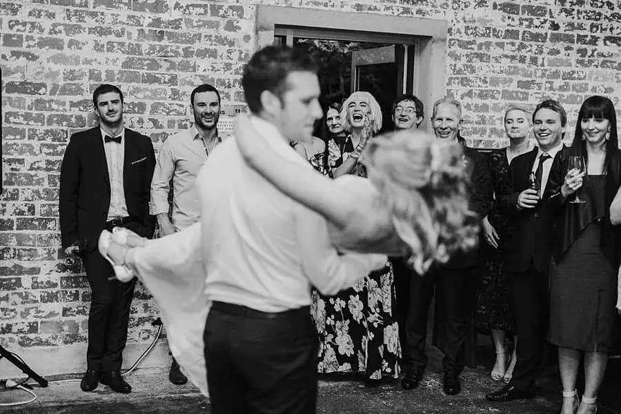 Black-and-white photograph of the groom supporting the bride as she leans backward while dancing.