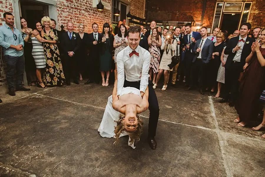 Groom supporting the bride in a deep backward dip while guests smile around them.