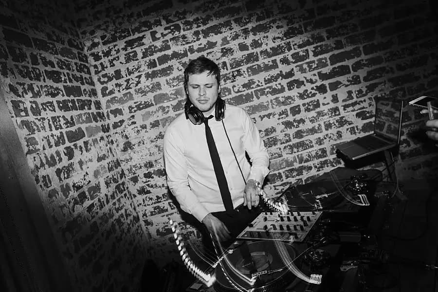 Black-and-white photograph of a DJ operating a mixing console.