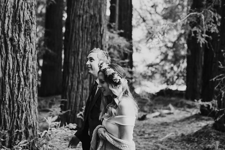 Black-and-white portrait of a couple standing beside a broad redwood trunk.