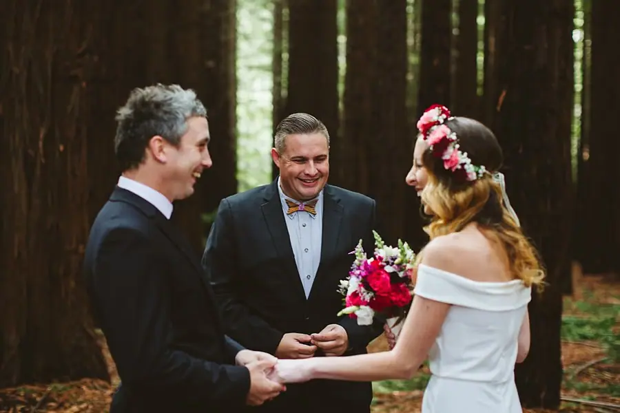 Bride and groom holding hands during their forest ceremony as the celebrant looks on.